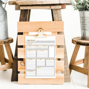 May include: A daily planner with a yellow and brown colour scheme is clipped to a wooden frame. The planner has sections for daily tasks, meal planning, and notes. The frame is sitting on a wooden stool.