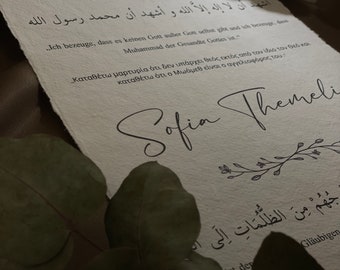 Könnte beinhalten: Ein weißes Zertifikat mit goldenen Akzenten, das einen arabischen Text und den Text "Zertifikat zur Konversion" sowie das Datum "28/05/2021" enthält. Das Zertifikat ist von "Sofia Themeli" unterzeichnet und enthält den Text "Ich bezeuge, dass es keinen Gott außer Gott selbst gibt und ich bezeuge, dass Muhammad der Gesandte Gottes ist."