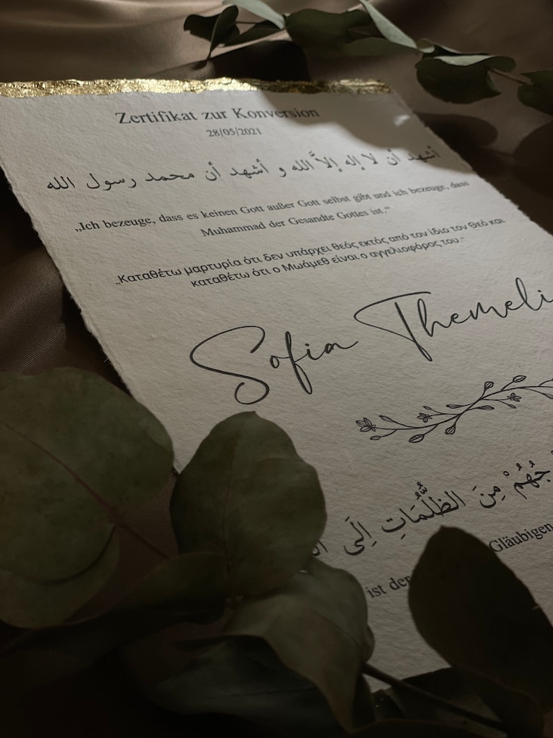 May include: A white certificate with gold accents, featuring an Arabic text and the text "Zertifikat zur Konversion" (German for "Certificate of Conversion") and the date "28/05/2021". The certificate is signed "Sofia Themeli" and includes the text "Ich bezeuge, dass es keinen Gott au&szlig;er Gott selbst gibt und ich bezeuge, dass Muhammad der Gesandte Gottes ist." (German for "I testify that there is no god but God and I testify that Muhammad is the Messenger of God.")