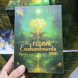 Close-up of the Floral Enchantments Tarot cards box featuring a glowing golden lotus on a mystical green background, symbolizing spiritual growth and inner magic. This elegant botanical tarot deck combines floral symbolism with enchanting artwork, perfect for tarot readers, nature lovers, and collectors of fantasy-inspired decks.