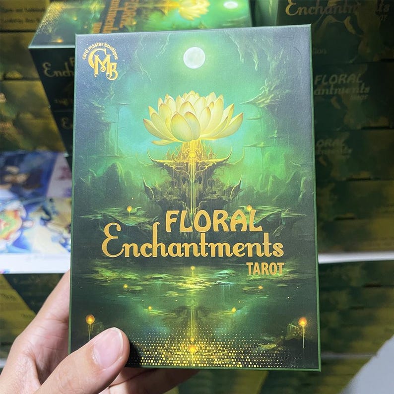Close-up of the Floral Enchantments Tarot cards box featuring a glowing golden lotus on a mystical green background, symbolizing spiritual growth and inner magic. This elegant botanical tarot deck combines floral symbolism with enchanting artwork, perfect for tarot readers, nature lovers, and collectors of fantasy-inspired decks.