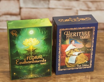 May include: Two tarot card boxes. One is green with "Floral Enchantments Tarot" in gold lettering and a lotus flower illustration. The other is blue with "Heritage Tarot" and a portrait illustration.