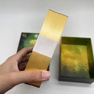 Side view of the Floral Enchantments Tarot deck held in hand, showing gold gilded edges and the thickness of the cards.