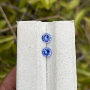Puede incluir: Dos gemas azules redondas y facetadas se muestran sobre una superficie blanca. Las gemas tienen un color azul claro vibrante y se colocan sobre un fondo neutro, resaltando su brillo. Las gemas son probablemente para la fabricaci&oacute;n de joyas.