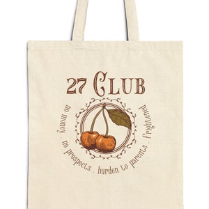 May include: A beige tote bag with a brown graphic of two cherries and the text "27 CLUB" with the phrase "know you on no prospects, burden to parents, frightened" surrounding the cherries.