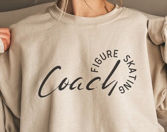 May include: A beige sweatshirt with the text "Coach" in a cursive font and a circle around it that says "Figure Skating".
