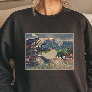 May include: Black sweatshirt with a graphic print of a Korean flag with a pagoda and mountains in the background.