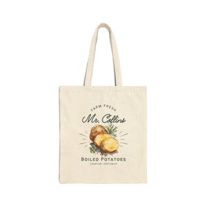 May include: A beige tote bag with a design featuring a watercolor illustration of boiled potatoes, a sprig of dill, and the text "Farm Fresh Mr. Collins Boiled Potatoes Exemplary Vegetables".