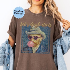 May include: Brown t-shirt with the text "Let's Gogh Girls" above a framed image of Vincent van Gogh wearing heart-shaped sunglasses and blowing a bubble. The shirt has a Comfort Colors® tag.