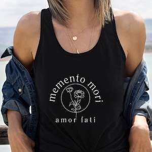 May include: A black tank top with a white graphic design that says "memento mori" in a circle with a flower inside. Below the circle, it says "amor fati".