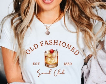 May include: White t-shirt with a brown graphic of an old fashioned cocktail with a cherry and the text "Old Fashioned Est 1880 Social Club".