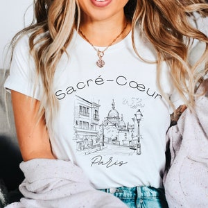 May include: White t-shirt with a black and white illustration of the Sacré-Cœur Basilica in Paris, France. The text "Sacré-Cœur Paris" is printed on the shirt.