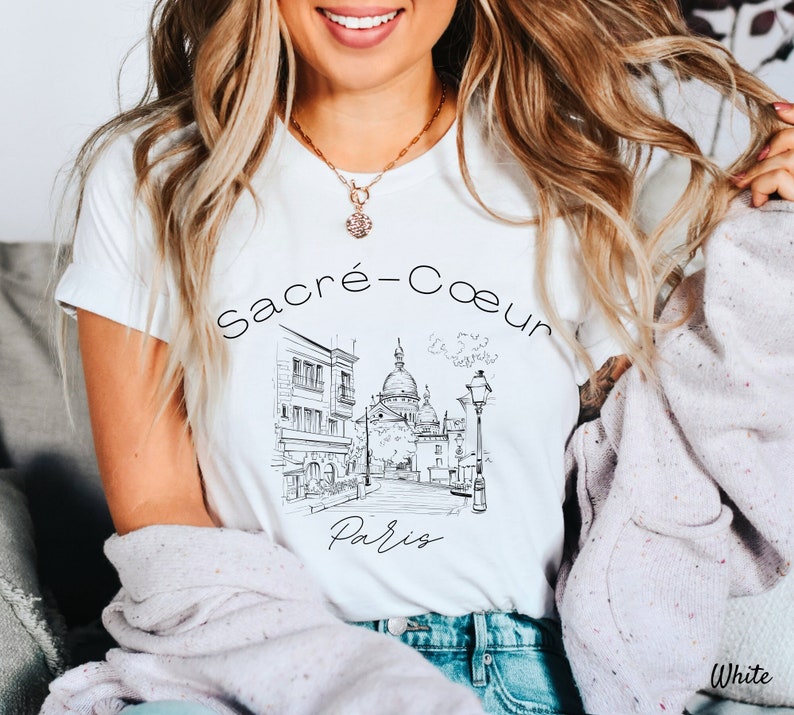 May include: White t-shirt with a black and white illustration of the Sacré-Cœur Basilica in Paris, France. The text "Sacré-Cœur Paris" is printed on the shirt.