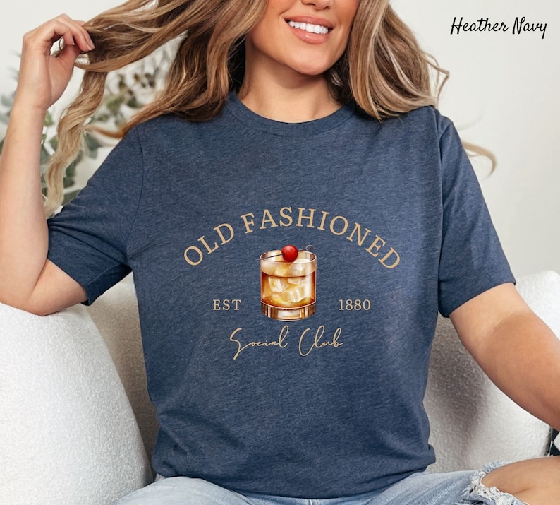 Puede incluir: Una camiseta azul marino jaspeada con un gr&aacute;fico de un c&oacute;ctel old fashioned con una cereza en la parte superior. El texto "Old Fashioned" est&aacute; por encima del c&oacute;ctel y "Est 1880 Social Club" est&aacute; por debajo del c&oacute;ctel.