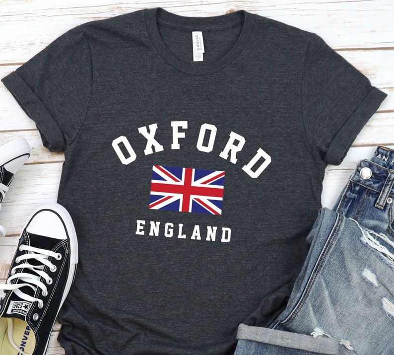 Puede incluir: Una camiseta gris oscuro con el texto "OXFORD ENGLAND" en letras blancas. Una peque&ntilde;a bandera del Reino Unido est&aacute; centrada sobre el texto.