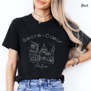 K&ouml;nnte beinhalten: Schwarzes T-Shirt mit einer wei&szlig;en Strichzeichnung der Basilika Sacr&eacute;-C&oelig;ur in Paris. Der Text "Sacr&eacute;-Coeur Paris" ist in einer Schreibschrift geschrieben. Das Shirt hat einen klassischen Rundhalsausschnitt.
