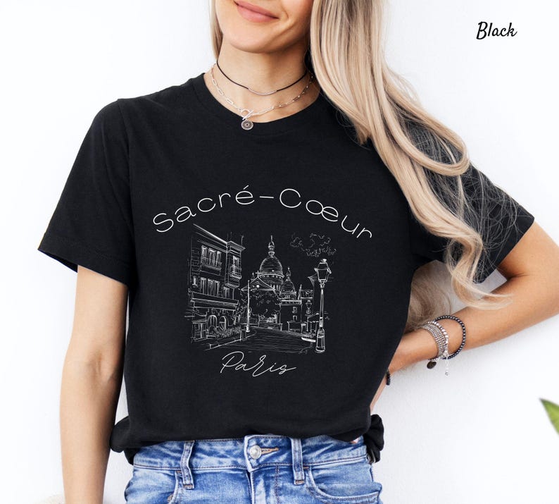 K&ouml;nnte beinhalten: Schwarzes T-Shirt mit einer wei&szlig;en Strichzeichnung der Basilika Sacr&eacute;-C&oelig;ur in Paris. Der Text "Sacr&eacute;-Coeur Paris" ist in einer Schreibschrift geschrieben. Das Shirt hat einen klassischen Rundhalsausschnitt.