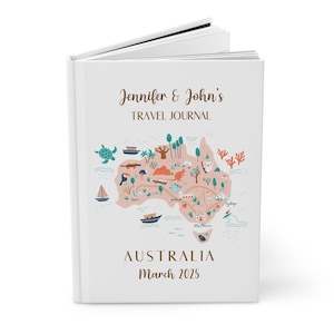 Puede incluir: Un diario de viaje blanco con el texto "Jennifer & John's TRAVEL JOURNAL" en escritura marrón. La portada presenta un mapa de Australia con ilustraciones de animales, árboles y barcos. La palabra "AUSTRALIA" y la fecha "Marzo 2025" también están impresas en la portada.