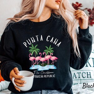 May include: Black sweatshirt with a white graphic of pink flamingos and palm trees. The text "Punta Cana" and "The Caribbean Dominican Republic" is printed on the sweatshirt.