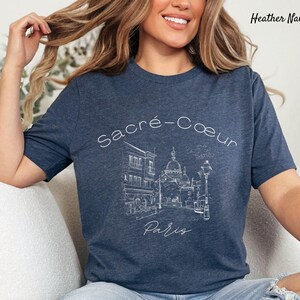 K&ouml;nnte beinhalten: Heather-Marineblaues T-Shirt mit einer wei&szlig;en Strichzeichnung der Basilika Sacr&eacute;-C&oelig;ur in Paris. Der Text "Sacr&eacute;-Coeur Paris" befindet sich &uuml;ber der Illustration. Das Shirt hat einen Rundhalsausschnitt und kurze &Auml;rmel.