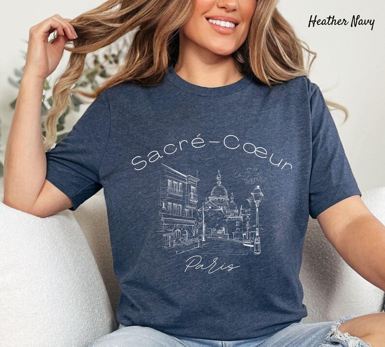 K&ouml;nnte beinhalten: Heather-Marineblaues T-Shirt mit einer wei&szlig;en Strichzeichnung der Basilika Sacr&eacute;-C&oelig;ur in Paris. Der Text "Sacr&eacute;-Coeur Paris" befindet sich &uuml;ber der Illustration. Das Shirt hat einen Rundhalsausschnitt und kurze &Auml;rmel.