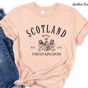 May include: Heather peach coloured t-shirt with black text that reads "Scotland" with a crest and the words "Est. 1707 United Kingdom" underneath.