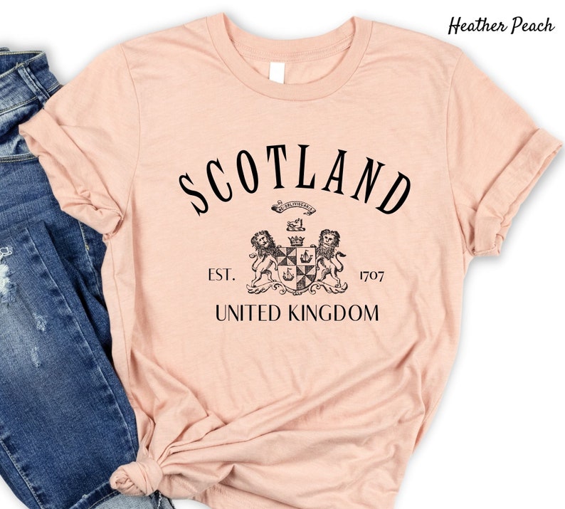 May include: Heather peach coloured t-shirt with black text that reads "Scotland" with a crest and the words "Est. 1707 United Kingdom" underneath.