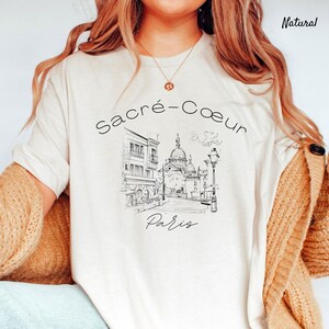 K&ouml;nnte beinhalten: Cremefarbenes T-Shirt mit einer Schwarz-Wei&szlig;-Skizze der Basilika Sacr&eacute;-C&oelig;ur in Paris. Der Text "Sacr&eacute;-Coeur Paris" ist &uuml;ber und unter der Illustration angeordnet. Das Shirt hat eine lockere Passform und kurze &Auml;rmel.