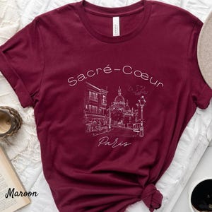 K&ouml;nnte beinhalten: Burgunderfarbenes T-Shirt mit einer wei&szlig;en Strichzeichnung der Basilika Sacr&eacute;-C&oelig;ur in Paris und dem Text "Sacr&eacute;-C&oelig;ur Paris". Das T-Shirt ist aus weichem Material und hat einen klassischen Rundhalsausschnitt.