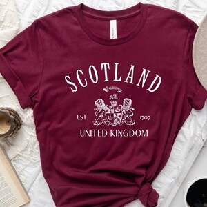 May include: Burgundy t-shirt with a white graphic of a crest and the text "Scotland Est. 1707 United Kingdom".