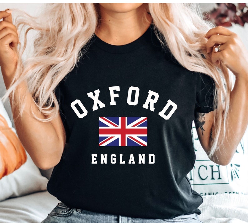 Puede incluir: Camiseta negra con texto blanco que dice "Oxford England" y una peque&ntilde;a bandera del Reino Unido.