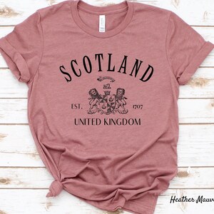 May include: Heather mauve t-shirt with black text that reads "Scotland Est. 1707 United Kingdom" and a black and white crest with two lions.
