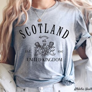 May include: Grey t-shirt with black text that reads "Scotland Est. 1707 United Kingdom" and a black and white illustration of a coat of arms.