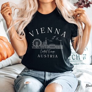May include: Black t-shirt featuring a white graphic design of the Vienna skyline, including the Ferris wheel, St. Stephen's Cathedral, and the text "Vienna, Central Europe, Austria".