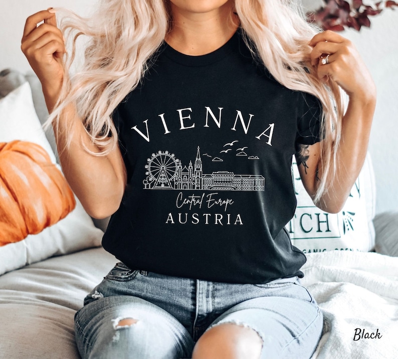 May include: Black t-shirt featuring a white graphic design of the Vienna skyline, including the Ferris wheel, St. Stephen's Cathedral, and the text "Vienna, Central Europe, Austria".