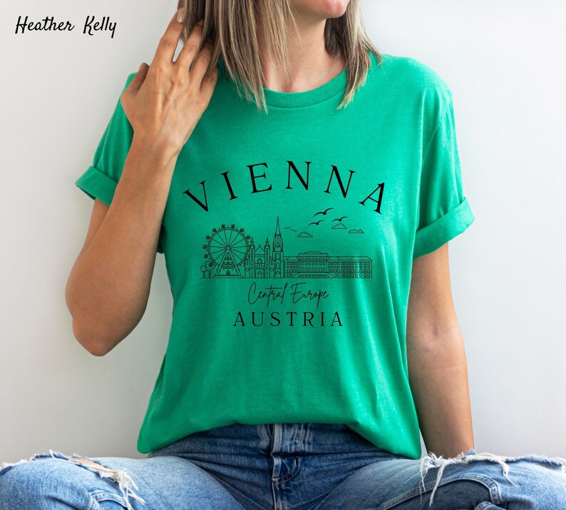 May include: A green t-shirt featuring a black graphic design of the Vienna skyline, including the Ferris wheel, St. Stephen's Cathedral, and the Hofburg Palace. The text "VIENNA", "Central Europe", and "AUSTRIA" is also included in the design.