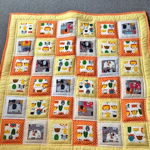 May include: A handmade baby quilt with a patchwork design. The quilt features squares with animal prints, including elephants, lions, and giraffes, set against a yellow and orange background. The quilt is bordered with a yellow fabric.