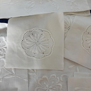 May include: A selection of white embroidered linens, possibly napkins or doilies. The designs include floral and butterfly patterns, with detailed embroidery and cutwork. The linens are displayed on a surface, highlighting the range of designs and textures.