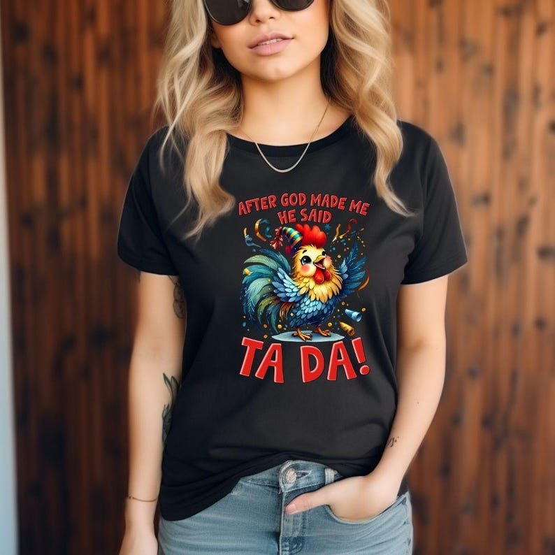 Puede incluir: Camiseta negra con un gallo de dibujos animados colorido y el texto "AFTER GOD MADE ME HE SAID TA DA!". El gallo tiene plumas azules, amarillas, rojas y verdes. La camiseta la lleva una persona.