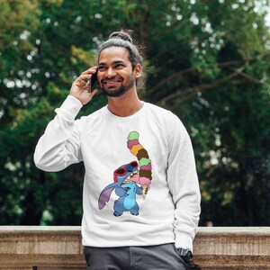 以下が含まれることがあります： 青い漫画のキャラクターがサングラスをかけて、カラフルなアイスクリームコーンを持っている白いスウェットシャツ。キャラクターはディズニー映画リロ＆スティッチのスティッチです。