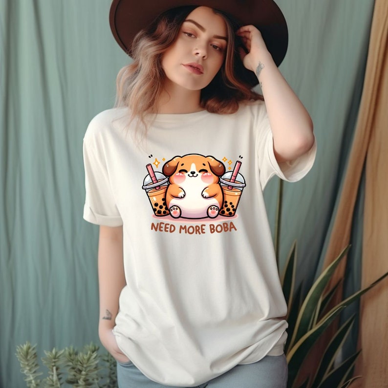 May include: White t-shirt with a cartoon dog holding two cups of boba tea. The text "NEED MORE BOBA" is printed below the dog.