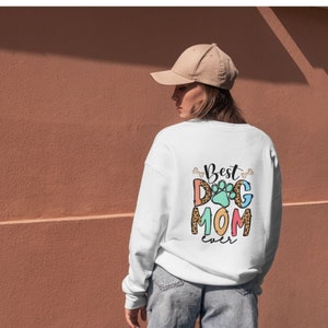 May include: White sweatshirt with the text "Best Dog Mom Ever" in colorful letters with a paw print graphic. The text is surrounded by bone graphics.