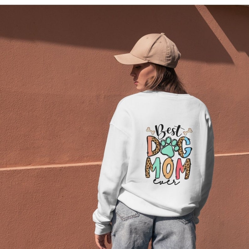 May include: White sweatshirt with the text "Best Dog Mom Ever" in colorful letters with a paw print graphic. The text is surrounded by bone graphics.
