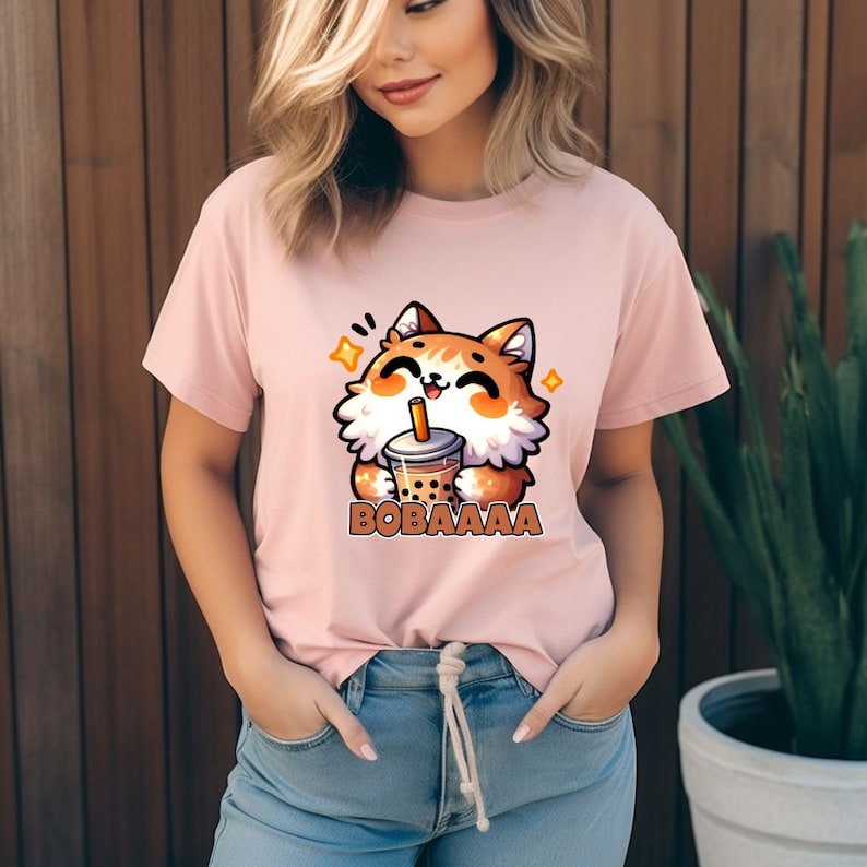 May include: A pink t-shirt with a cartoon illustration of a brown and orange cat holding a boba tea cup. The text "BOBAAAAA" is printed below the cat.