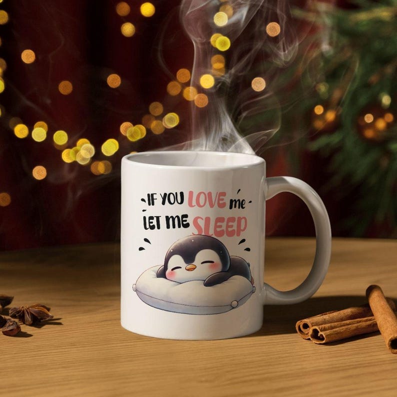 Puede incluir: Taza de cer&aacute;mica blanca con asa, con un ping&uuml;ino de dibujos animados durmiendo sobre una almohada. La taza tiene el texto "If you love me - Let me sleep" en negro y rosa. Sale vapor de la taza.