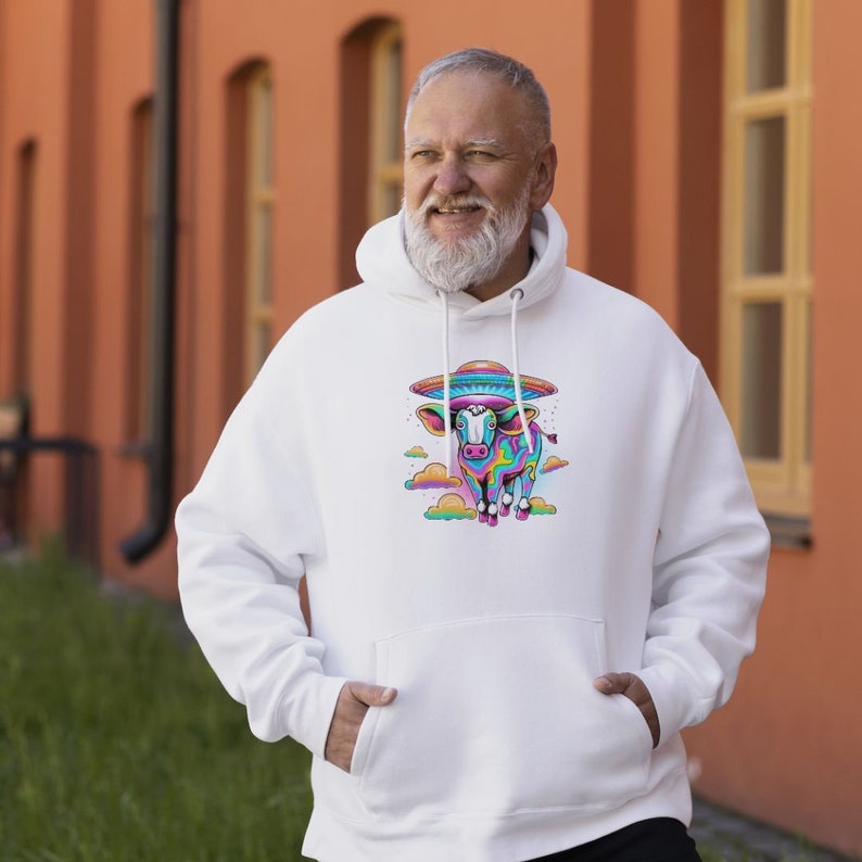May include: A white hooded sweatshirt featuring a colourful graphic of a cow wearing a UFO hat. The cow is surrounded by clouds and is in a psychedelic colour scheme.