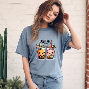 May include: A light blue t-shirt with a graphic of two cartoon bubble tea cups. The text "BEST TEAS" and "#BESTIES" is printed on the shirt.