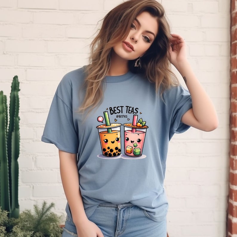 May include: A light blue t-shirt with a graphic of two cartoon bubble tea cups. The text "BEST TEAS" and "#BESTIES" is printed on the shirt.