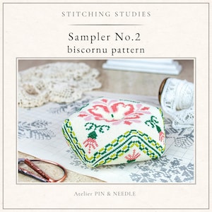 Może przedstawiać: Kwadratowy sampler z wzorem biscornu z haftem kwiatowym w kolorze różowym, zielonym i białym. U góry tekst "STITCHING STUDIES" i "Sampler No.2 biscornu pattern". Na dole tekst "Atelier PIN & NEEDLE".
