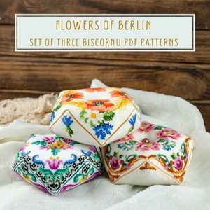 May include: Set of three floral embroidered biscornu pillow patterns. The patterns feature a variety of flowers in shades of pink, blue, yellow, and green.